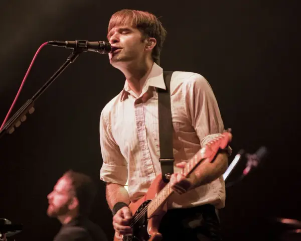 Ben Gibbard chante et joue de la guitare sur scène, éclairé par les projecteurs.