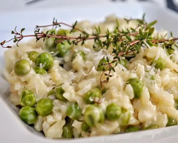 Kremowe risotto z groszkiem, posypane parmezanem i udekorowane gałązką tymianku. Pyszne danie, które zachwyca smakiem.