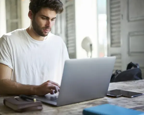 Mężczyzna w białej koszulce pisze na laptopie, przygotowując wniosek o urlop na poszukiwanie pracy.
