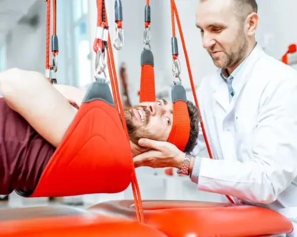 Fizjoterapeuta pomaga pacjentowi w terapii wiszącej, która może być jednym z zabiegów rehabilitacyjnych na kręgosłup lędźwiowy.
