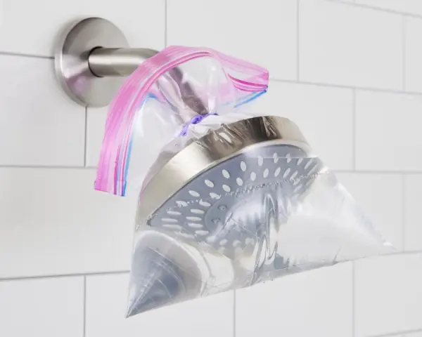 A shower head is submerged in a plastic bag filled with vinegar, secured with a rubber band. This shows how to clean shower head vinegar for a sparkling finish.