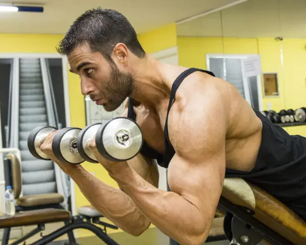Man utför spider curls med hantlar på ett gym.