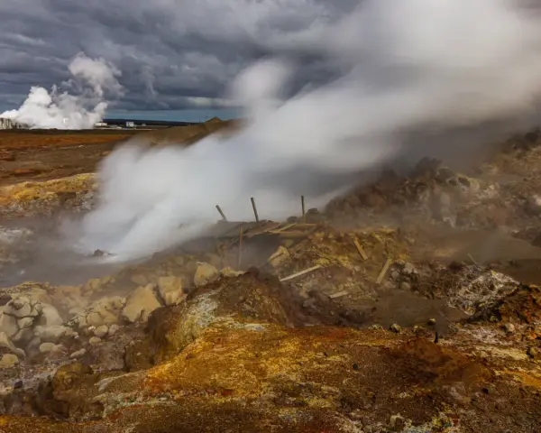 Gunnuhver hot springs: para buchująca z ziemi, zniszczona drewniana konstrukcja, chmury burzowe nad krajobrazem.