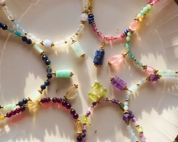 Kolorowe naszyjniki z kamieni szlachetnych, w tym lapis lazuli znak zodiaku, ułożone na talerzu.