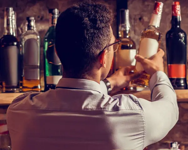 Mann wählt eine Flasche aus, in der reift Whisky in der Flasche nach. Viele Flaschen stehen im Regal.