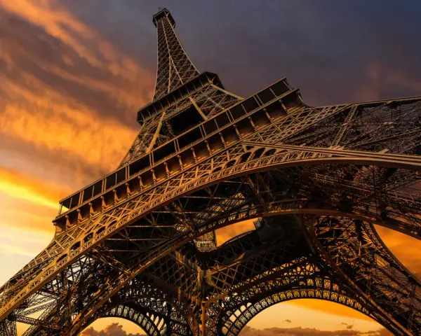 La Torre Eiffel, una icónica estructura de hierro forjado, se alza majestuosa contra un cielo anaranjado al atardecer.