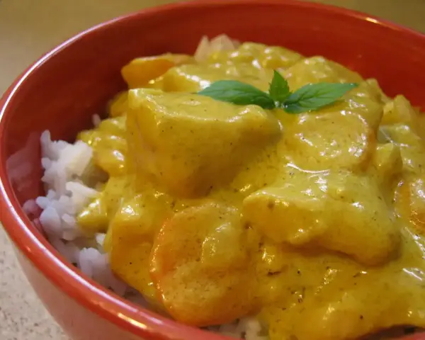 Miseczka ryżu z kurczakiem w kremowym sosie z curry, ozdobiona listkiem mięty.
