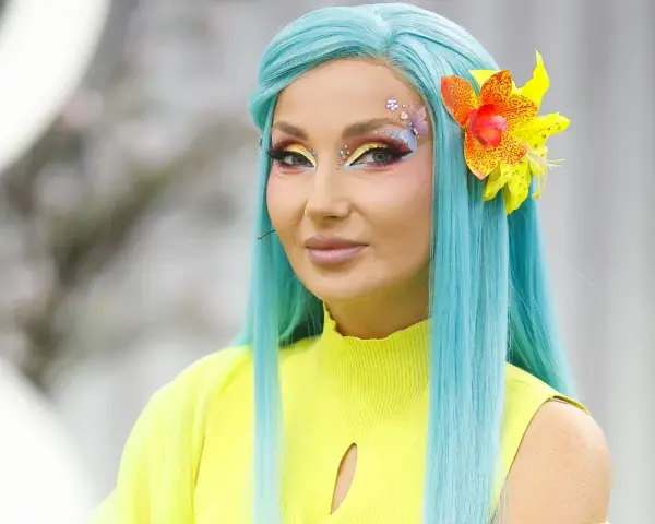 Cleo w turkusowej peruce i neonowym żółtym topie, z barwnym makijażem i kwiatem we włosach, zapowiada nową piosenkę.