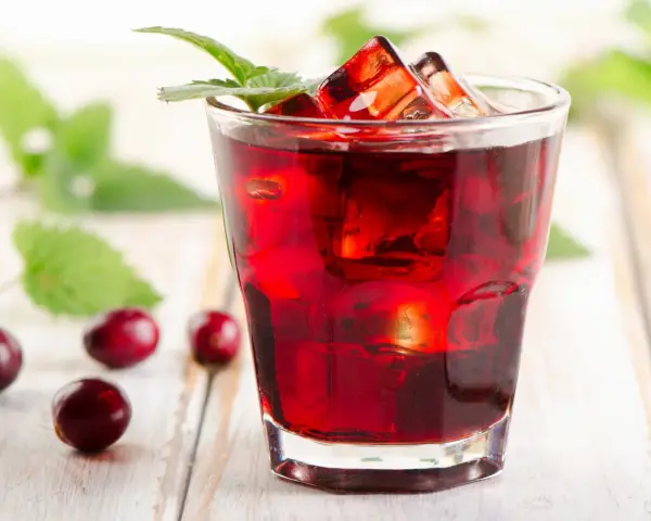 Orzeźwiający drink z żurawiną, lodem i listkiem mięty, otoczony kilkoma owocami żurawiny na drewnianym tle.