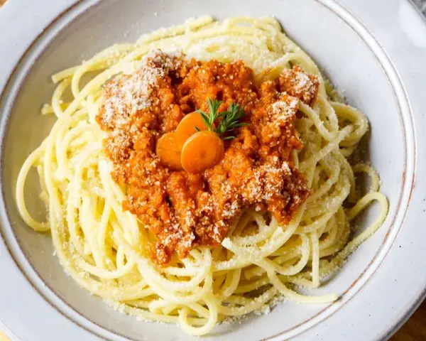 Spaghetti Bolognese, zubereitet im Thermomix, mit Karottenscheiben und Petersilie garniert.