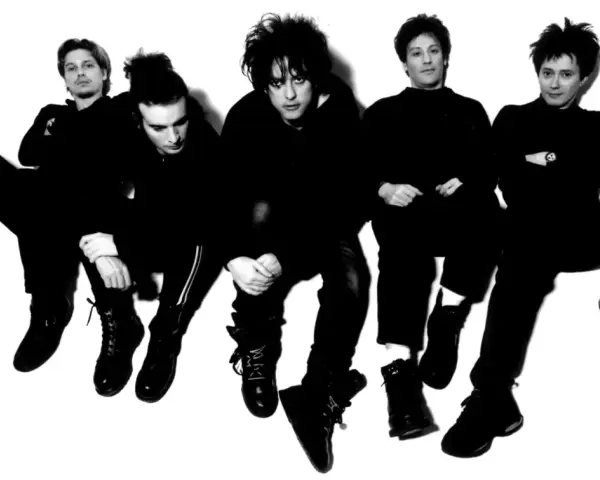 Les membres de The Cure, cinq silhouettes sombres aux coiffures distinctives, posent en groupe, l'air pensif.
