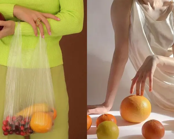 Mani che tengono una mela e una busta con ciliegie e arance. Altre arance e un limone sparsi su uno sfondo chiaro, evocando un'essenza di fruit extract.
