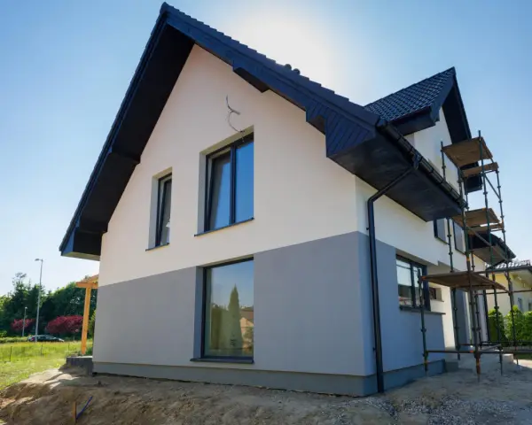 Nowy dom z dwukolorową elewacją, biało-szarą, to świetny pomysł na elewację domu. Widać rusztowania, co sugeruje trwające prace.