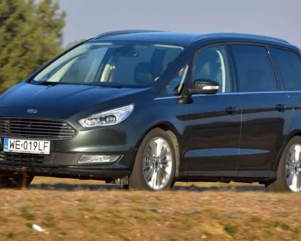 Ciemnozielony Ford Galaxy MK3 w ruchu, z polską tablicą rejestracyjną WE 019LF, przemierza wiejskie drogi.