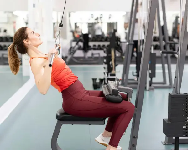 Kvinna tränar rakarmade latsdrag på gym.