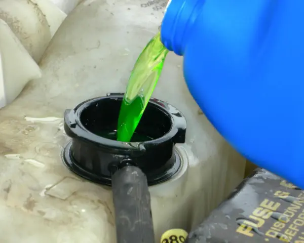 Green antifreeze is poured from a blue jug into a car's coolant reservoir. This raises the question: does antifreeze expire?