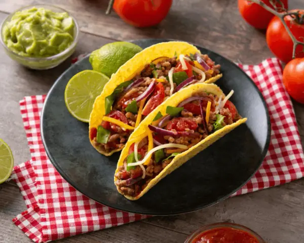 Dwa pyszne tacos z wołowiną, pomidorami, cebulą i serem, podane z limonką i guacamole.