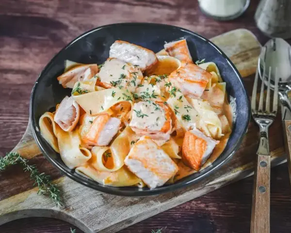 Herzhafte Bandnudeln mit saftigen Lachs-Stücken in cremiger Lachs Sahne Sauce, garniert mit frischen Kräutern. Ein Genuss!