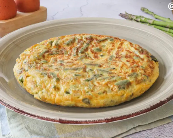 Tortilla de esparragos dorada y esponjosa, con trozos verdes de espárragos integrados en el huevo.