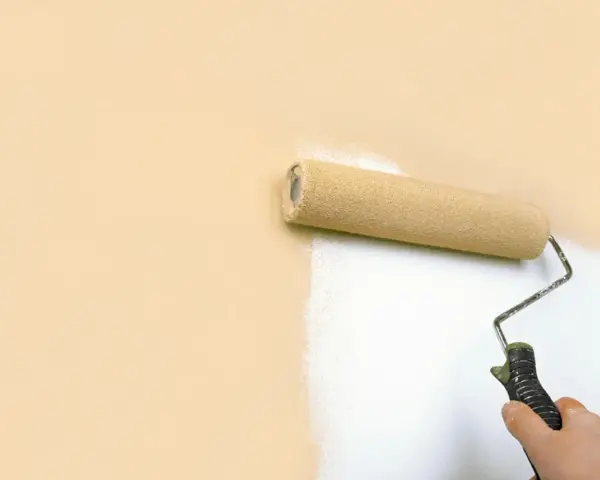 Rodillo pintando una pared de color melocotón con pintura blanca, buscando la mejor pintura antiruido para un hogar tranquilo.