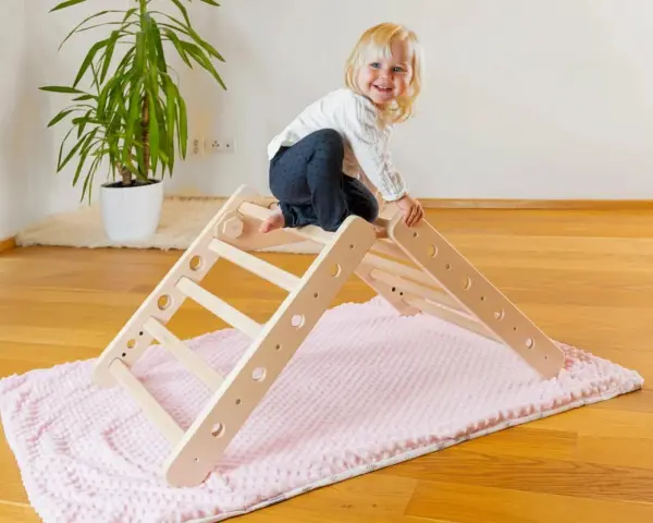 Ein fröhliches Kleinkind erkundet ein Pikler Dreieck. Ab wann Kinder damit spielen können, hängt von ihrer Entwicklung ab.