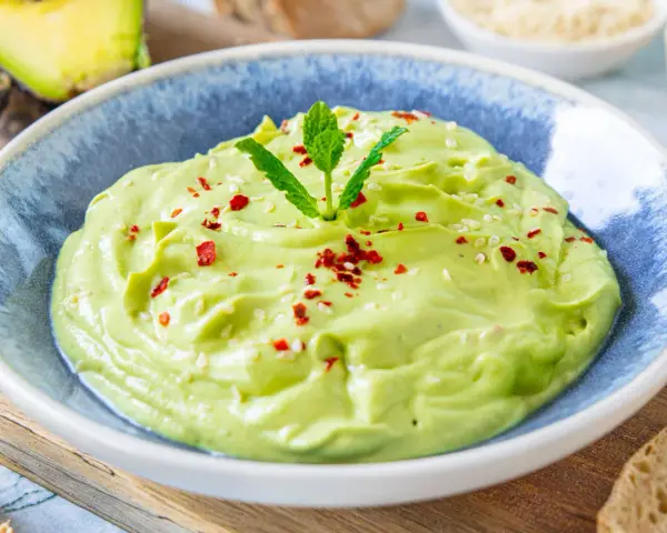 Cremige Avocado-Creme, garniert mit Minze, Sesam und Chiliflocken, serviert in einer blauen Schüssel. Perfekt als Dip oder Brotaufstrich.