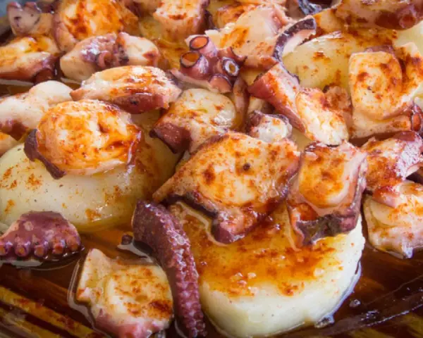 Pulpo a la gallega servido en plato de madera, con patatas cocidas y espolvoreado con pimentón.