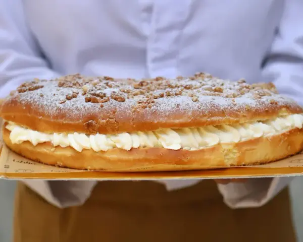 Deliciosa coca de San Juan rellena de crema, cubierta con azúcar glas y trocitos crujientes. ¡Perfecta para celebrar!