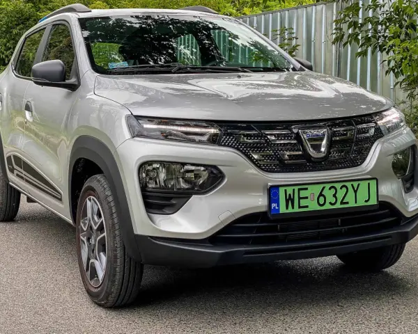 Srebrny Dacia Spring Electric z zieloną tablicą rejestracyjną WE 632YJ zaparkowany na drodze.