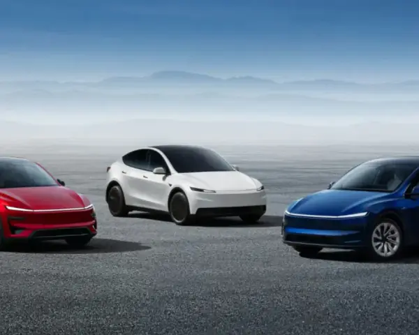 Trzy samochody Tesla: czerwony, biały i niebieski, stoją na pustej drodze z górami w tle.
