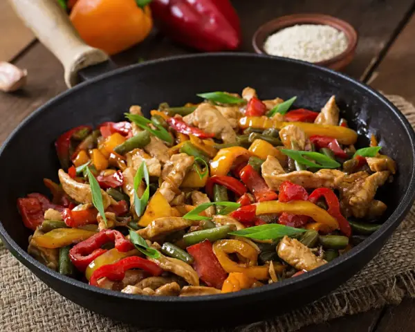 Straccetti di pollo con peperoni colorati e fagiolini, un piatto saporito e invitante servito in padella.