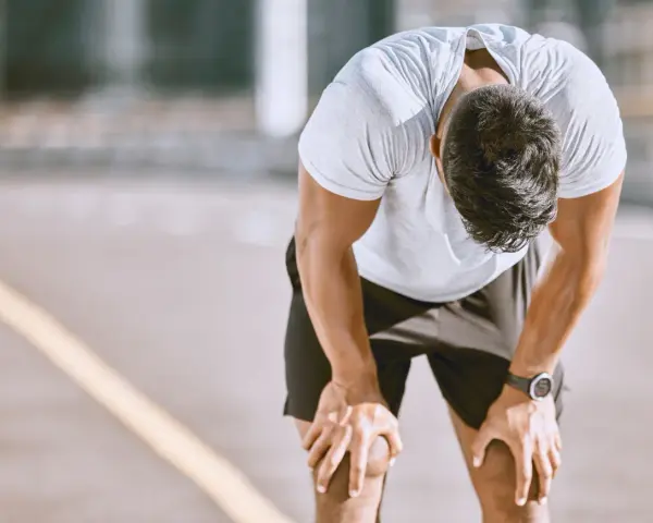 Atleta esausto con la testa china, mani sulle ginocchia, forse uno dei sintomi di overtraining.