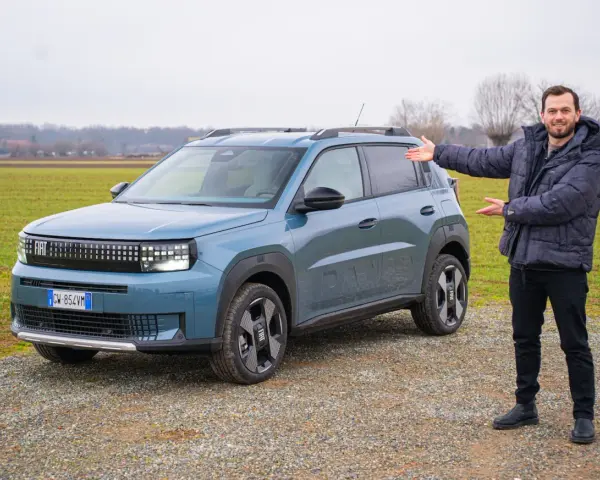 Mężczyzna prezentuje nowy, niebieski Fiat Grande Panda na tle zielonego pola.