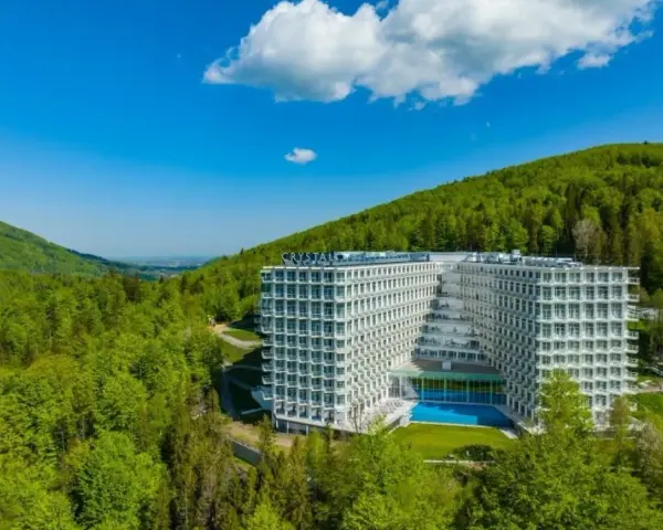 Nowoczesny Crystal Mountain Hotel Wisła otoczony zielonymi wzgórzami, z basenem i tarasami.