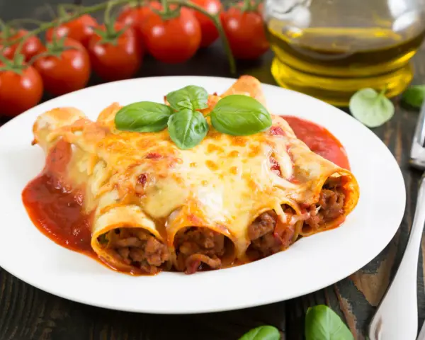Cannelloni kontra naleśniki z mięsem: zapieczone w sosie pomidorowym i serze, ozdobione bazylią. Obok pomidorki i oliwa.