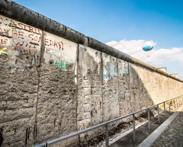 Beim Berlin Mauer besichtigen sieht man Graffiti und einen Heißluftballon.