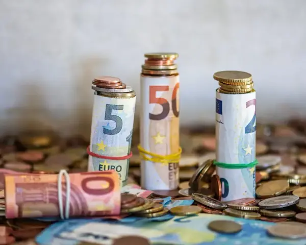 Zwijane banknoty euro i monety, symbolizujące kwotę darowizny wolną od podatku, tworzą stosy na tle innych monet.