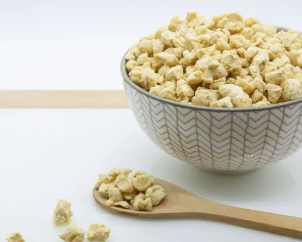 Un cuenco lleno de soja texturizada y una cuchara de madera con más de este ingrediente versátil.