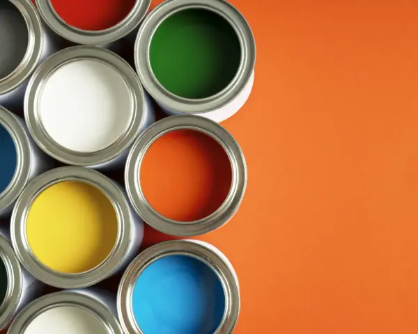 Un assortiment de pots de peinture glycero ou acrylique ouverts, révélant des couleurs vives comme le bleu, le jaune, le rouge, le vert et l'orange sur fond orange.