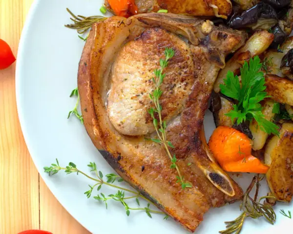 Une côte de porc savoureuse accompagnée de légumes rôtis, de pommes de terre et de tomates cerises.
