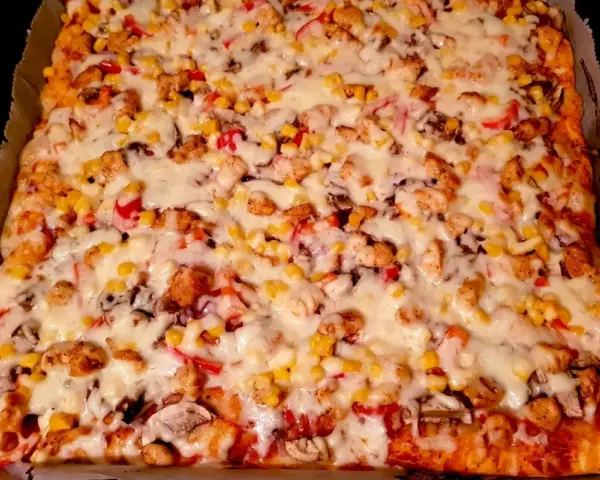 Pyszny przepis na pizzę z kurczakiem, kukurydzą i pieczarkami, obficie posypaną ciągnącym się serem.