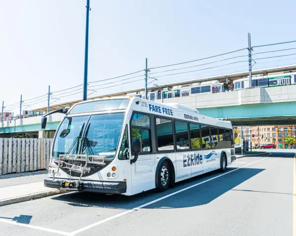 A white EZRide bus, offering fare-free transit from Boston to Cambridge, MA, drives past an elevated train station.