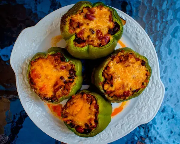 Cuatro pimientos verdes rellenos con carne, frijoles y arroz, cubiertos con queso derretido, servidos en un plato blanco.