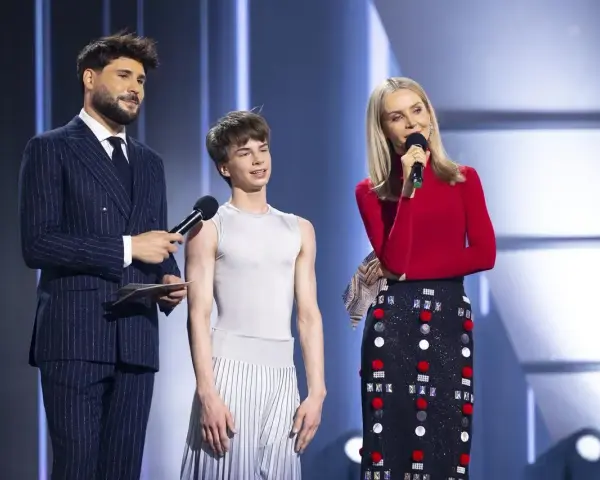 Tymek Sobczyk w białej koszulce i spodniach w paski, obok prowadzących program.