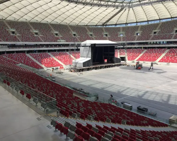 Przygotowania do koncertu Depeche Mode w Warszawie. Ogromny stadion z pustymi czerwonymi trybunami i sceną w budowie.