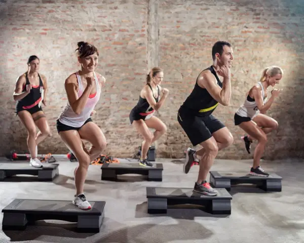 Un groupe de personnes participe à un cours step, effectuant des mouvements dynamiques sur des plateformes d'exercice dans une salle de sport.