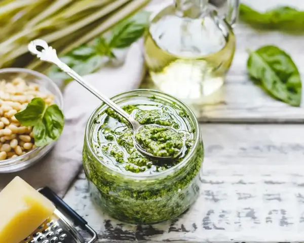 Un barattolo pieno di profumato pesto alla genovese, con pinoli, basilico e olio d'oliva pronti per essere mescolati.