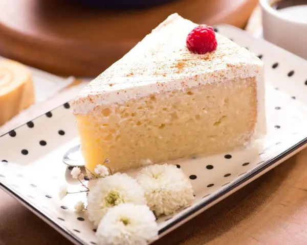 Pyszny kawałek ciasta Tres Leches, udekorowany maliną i cynamonem, czeka na spróbowanie. Idealny przepis na deser.