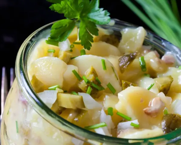Ein köstlicher Kartoffelsalat ohne Mayo, mit Gurken und frischen Kräutern, serviert in einem Glas.