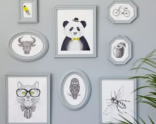 En samling gråa ramar med djur och föremål. En panda med fluga, en tjur, en katt med glasögon, en uggla, en bi, ett äpple och en cykel. Någon har valt att måla ramar för att skapa en personlig vägg.
